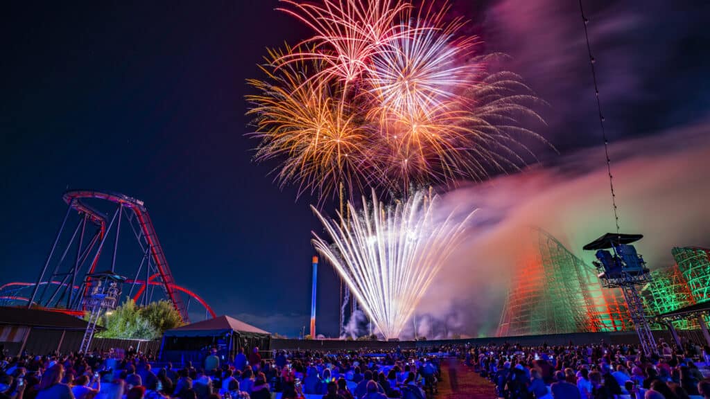 a huge fire works display at night over a roller coaster