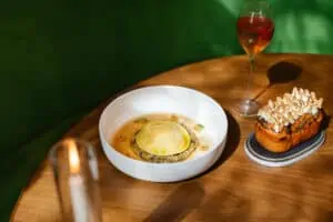 An ornate culinary dish set on a wood table with green leather seating.