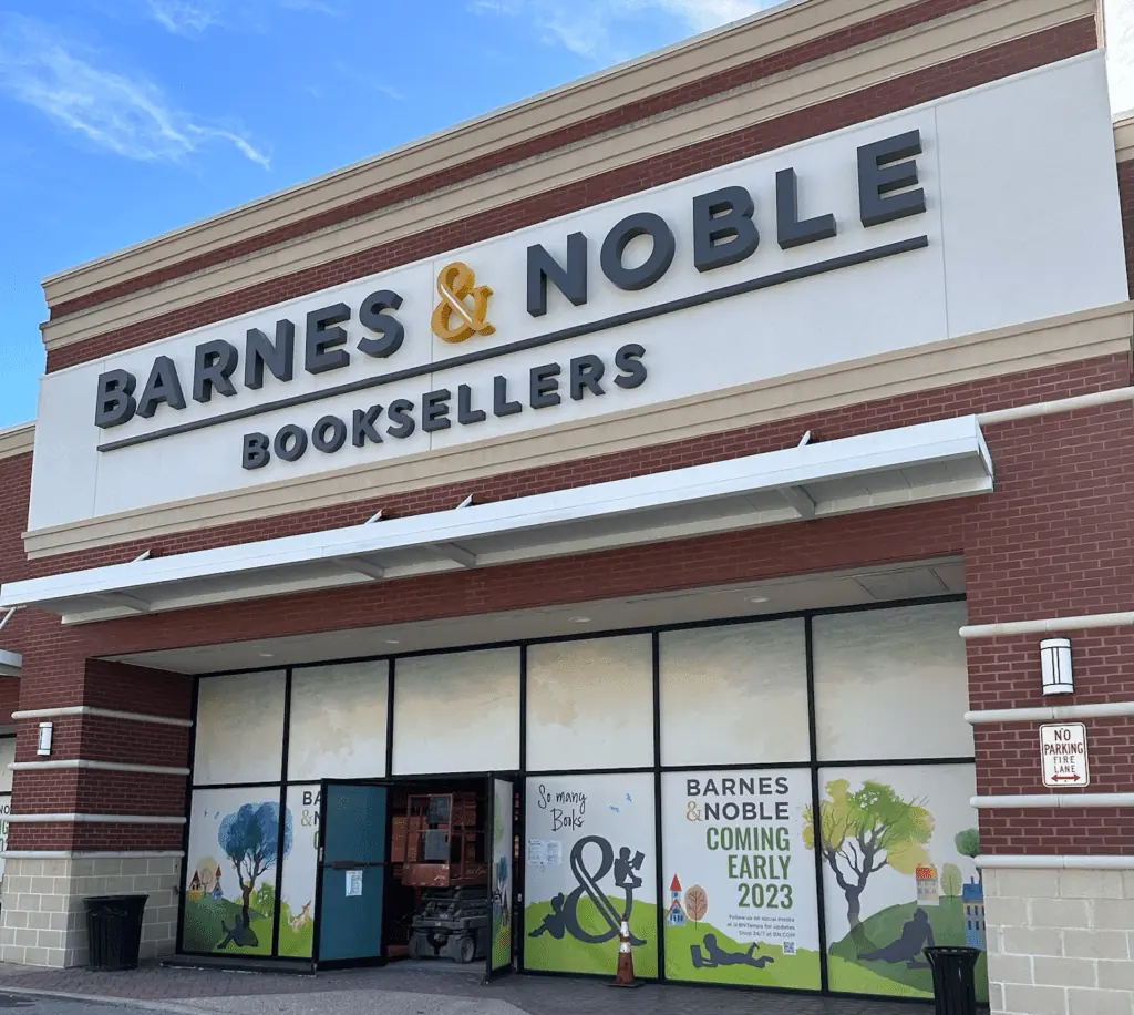 Exterior of a bookstore. A giant Barnes and Noble sign in black lettering with a gold "&" is at the center.