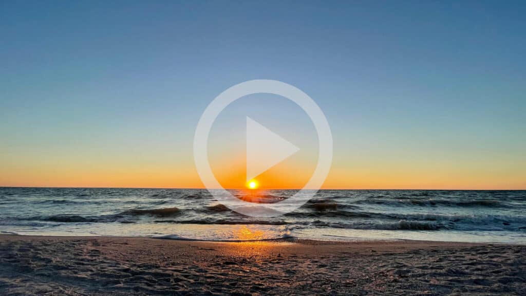 a beach at sunset with a "play" video button on it