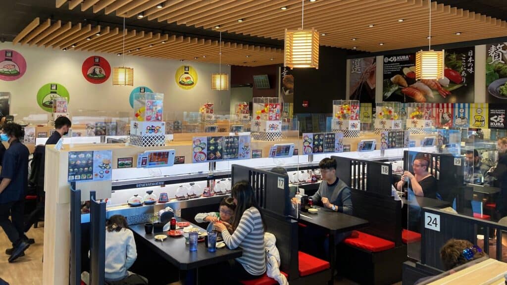 people dine at a sushi restaurant that delivers food via conveyer belt
