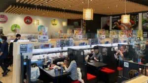 people dine at a sushi restaurant that delivers food via conveyer belt