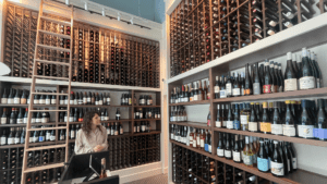 inside a wine shop. rows of assorted bottles are visible on the shelves. the general manager walks through and discusses different varieties.