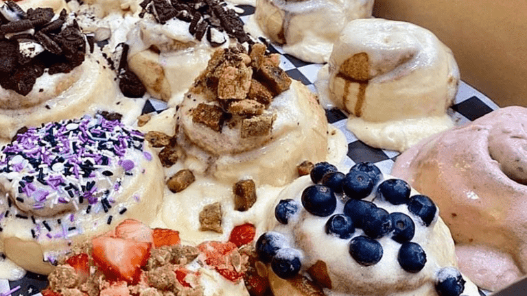 A group of cinnamon rolls covered in sprinkles and various fruits and frostings.