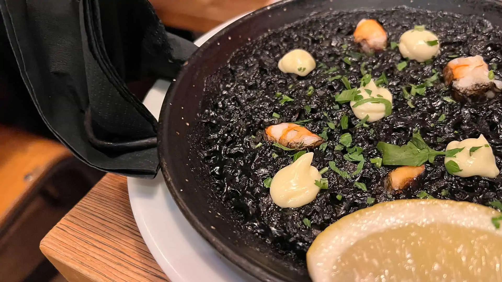 Black ink paella served on a iron dish with a slice of lemon at casual dining restaurant Lobos Tapas in Soho, London