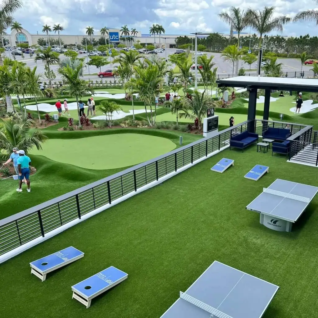 Several putting greens set up next to ping pong tables and corn hole boards. 