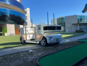 A roving golf cart is parked next to a miniature golf course.