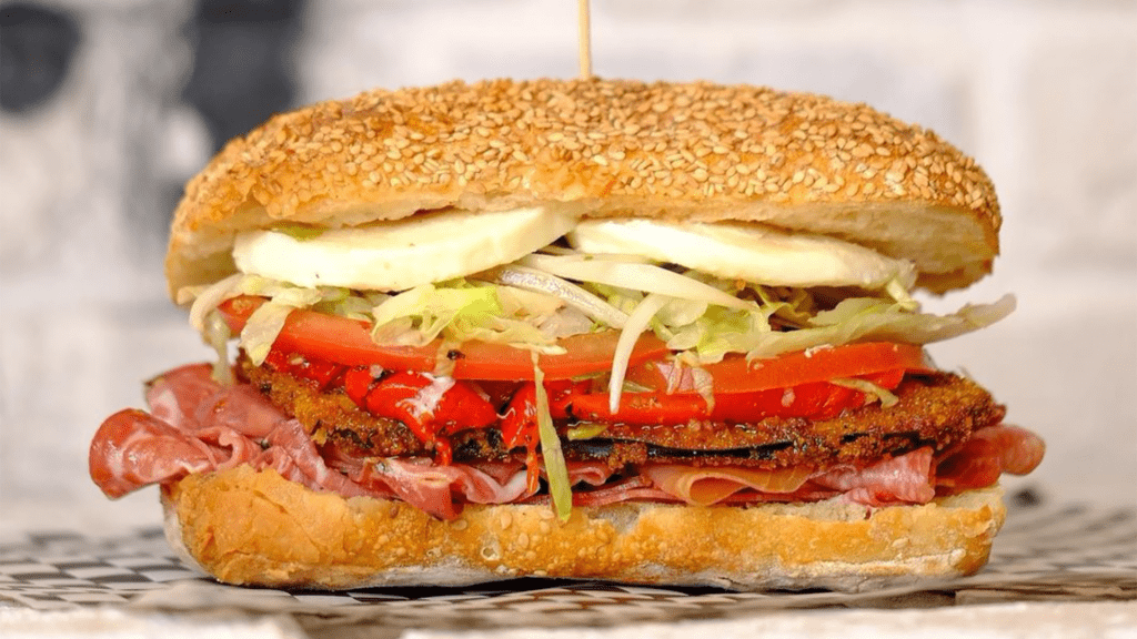 A small stacked sandwich with capicola, shredded lettuce and red peppers. 