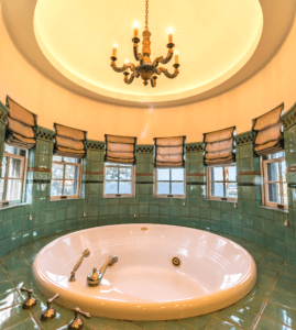 A bathroom jacuzzi tub with green tiles and windows surrounding the tub.