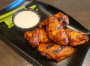 chicken wings covered in a bbq sauce on a black plate.