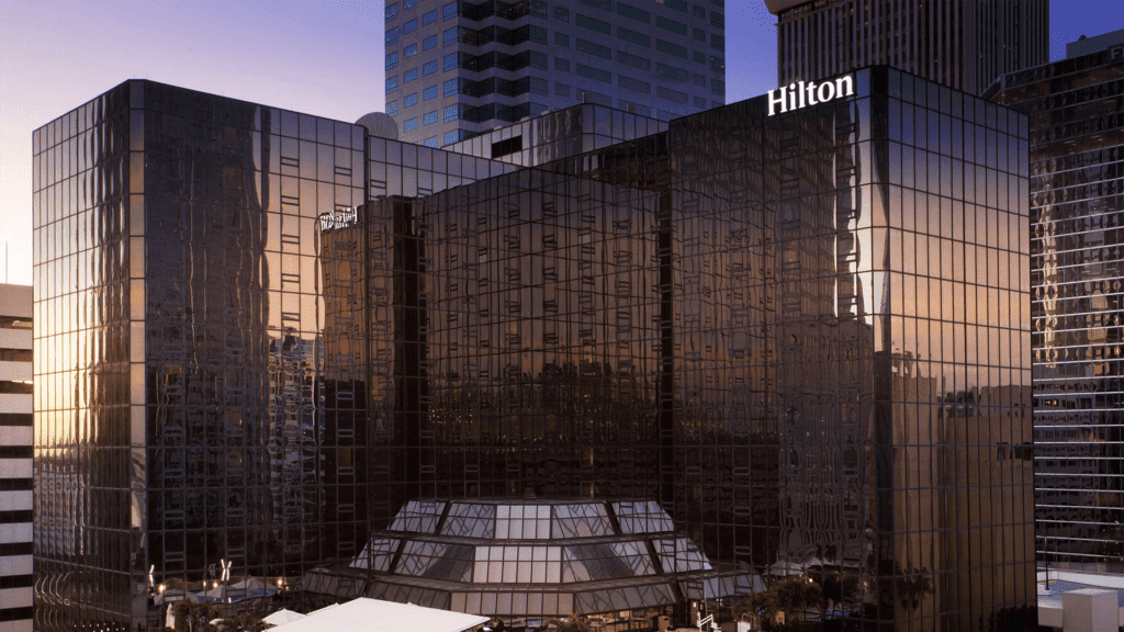 Exterior of a tall hotel in downtown Tampa. A glowing Hilton sign is on the top of the building.