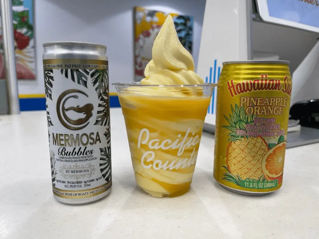 Two cans of soda set on either side of a yellow pineapple dole whip float. 