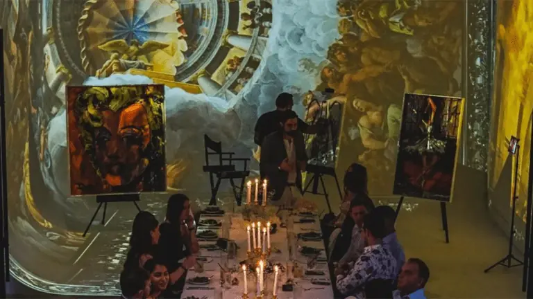 Projection mapping of surreal Salvador Dali paintings. A clock is melting on the wall. A table covered in white linen and candles is photographed from above.