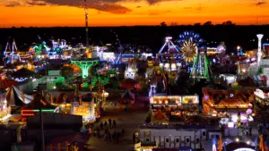 A large fairgrounds area. Carnival rides are lit up at sunset.