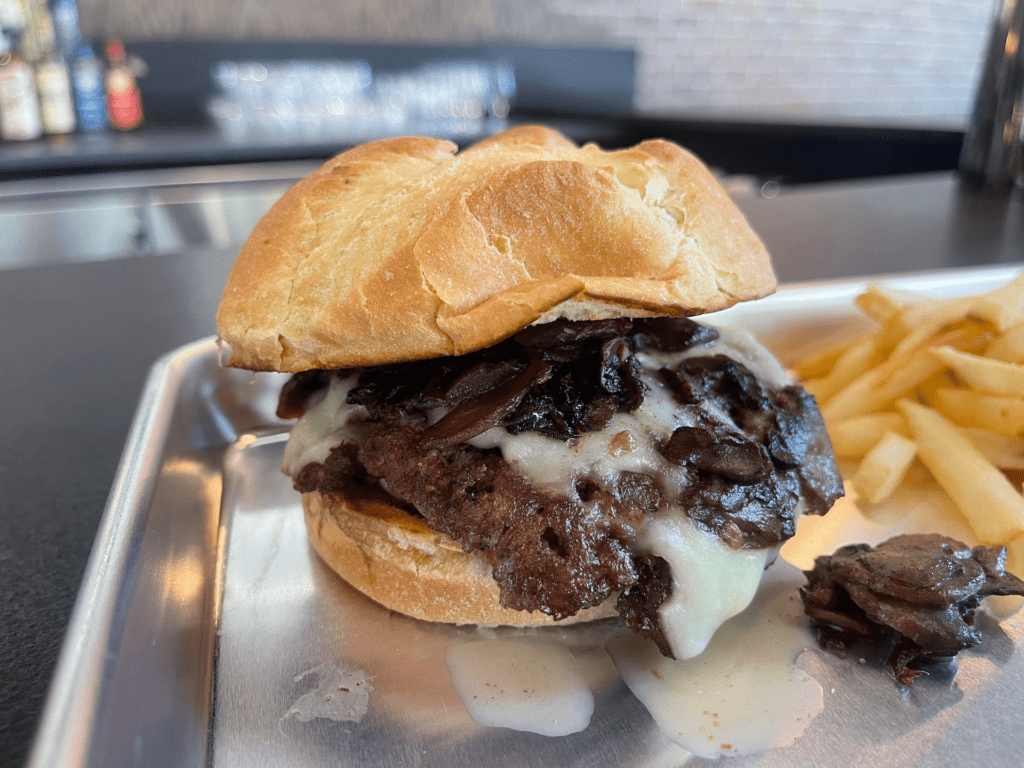 A burger covered in fresh provolone cheese and mushrooms. Golden fries are on the plate. 