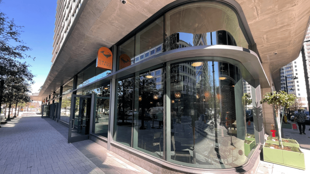 Exterior of a restaurant with full glass doors. A copper sign with a whale drawn on it hangs over the door.