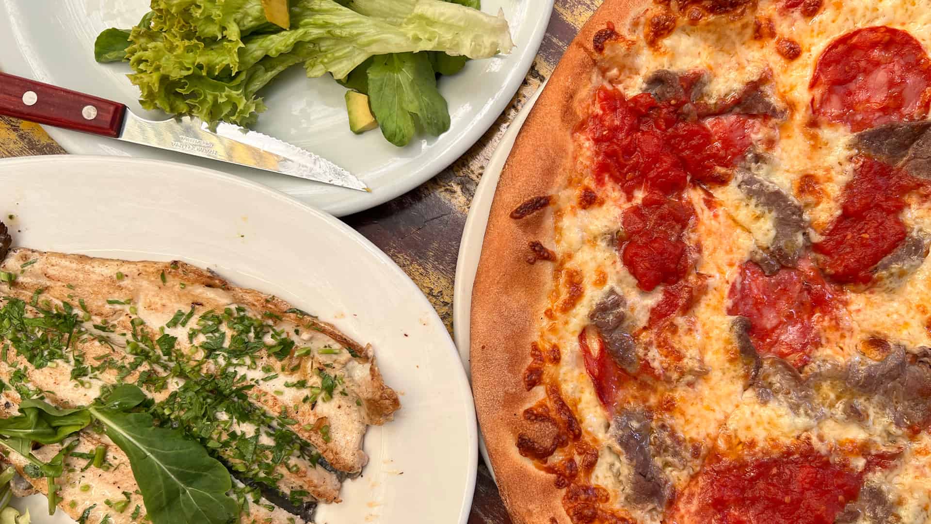 Plates of salad with whole grilled trout and a pizza with meat
