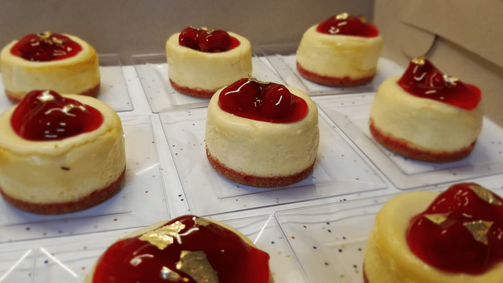 Assorted cheesecakes covered in red strawberry and cheery jam are placed on parchment paper. 