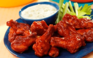 Buffalo wings, bright orange, on a plate with green veggies.