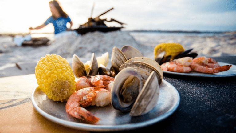 a plate of corn, shrimp and oysters on a plate on the beach