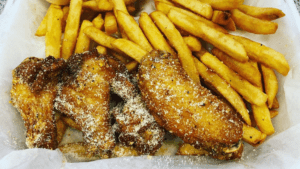 chicken wings covered in lemon pepper sauce on a plate with golden fries