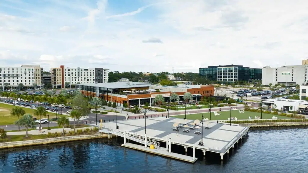 Aerial footage of a waterfront old hall with docks set on the waterfront. Green space surrounds the facility. 