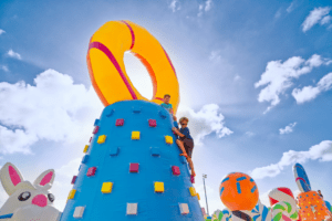 Large blue inflatable climbing wall. Two children are climbing to the top.
