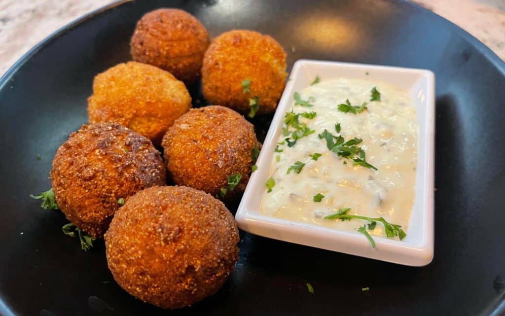 A plate of fried hush puppies with a spicy mayo dip on the side. 