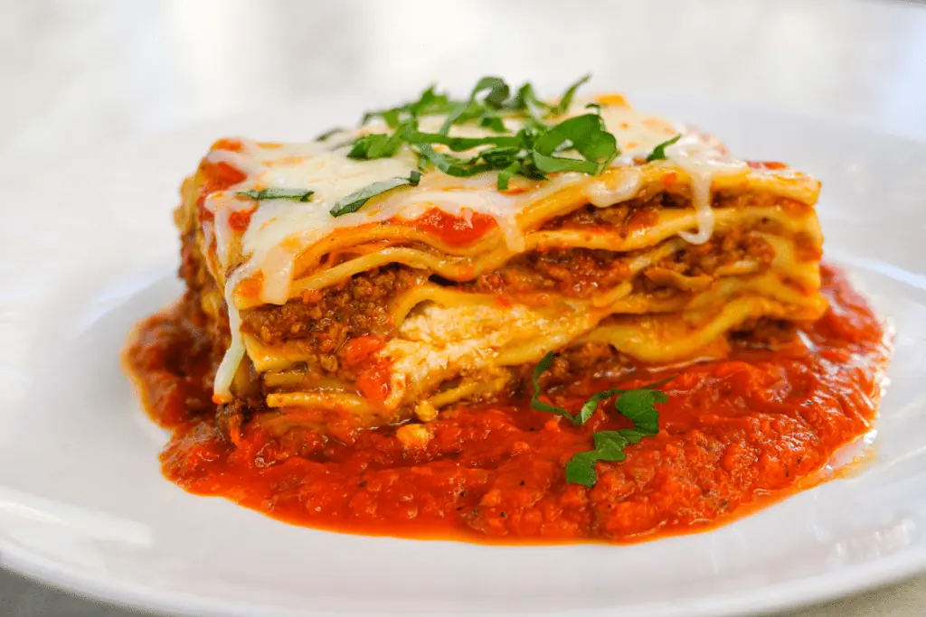A plat bof lasagna in meat sauce with green veggie garnishments. 