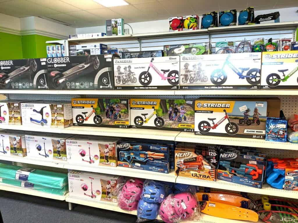 Shelves of bikes, scooters, bike helmets and skateboards inside of a toy shop. 