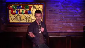 A man on a stage in a jacket performing standup comedy