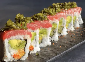 A plate of sushi topped with greens and drizzled with a light sauce.