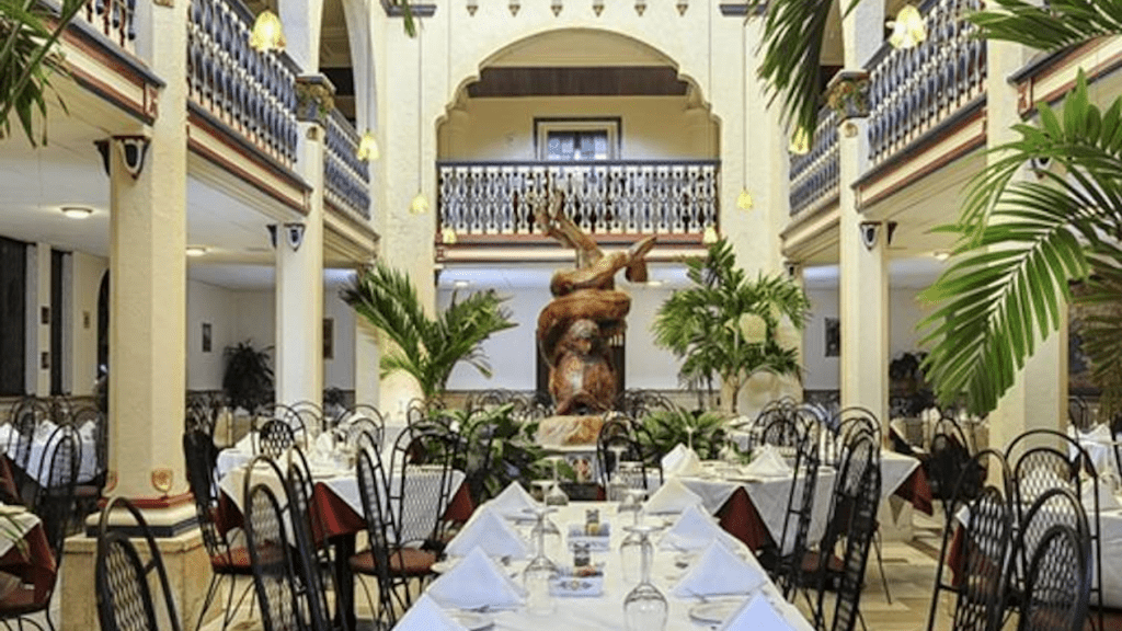 interior of a fine dining restaurant with white linen table and palm trees lining the dining room. 