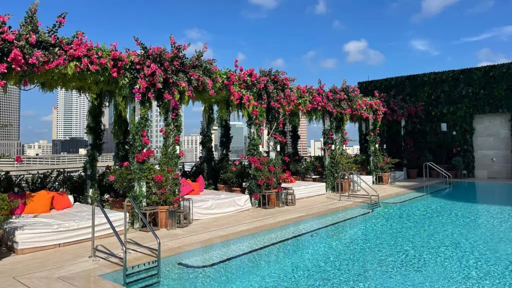 A ROOFTOP POOL WITH LUSH DAYBEDS SET NEXT TO THE POOL. THE day beds are shaded with ivy covered archways