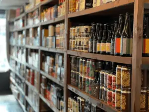 inside a bottle shop. Rows of cans of beer, wine bottles and more are visible on wooden shelves.