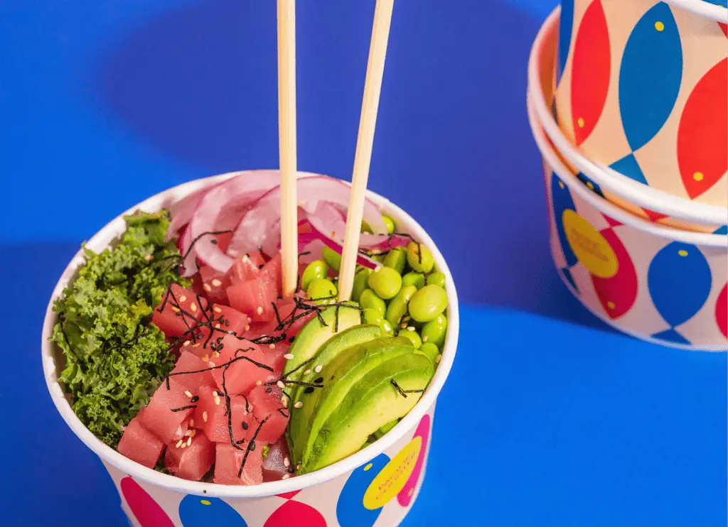 a bowl on a blue plate filled with green and red veggies, chopsticks stick out from the bowl