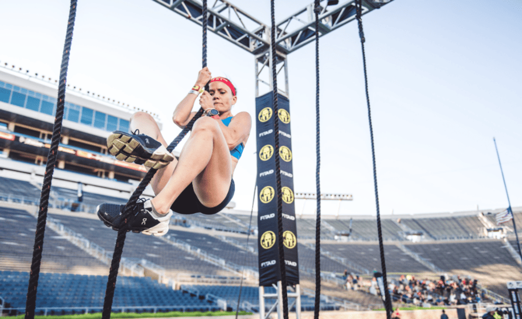 person climbing a rope course set up at the center of a large sports stadium