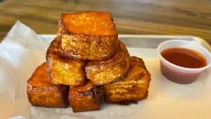 fried cheese cubes stacked like a pyramid on a plate next to a cup of red guava dipping sauce.