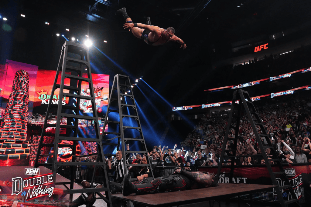 a man does a front flip off of a ladder onto another wrestler on a table. 