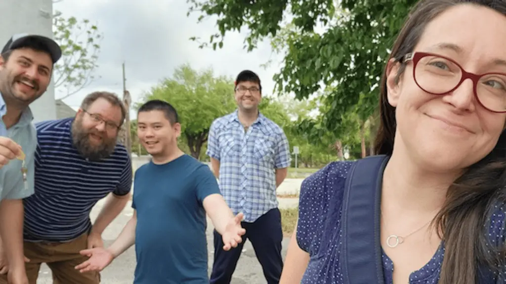 5 people stand together on a side street smiling at the camera.