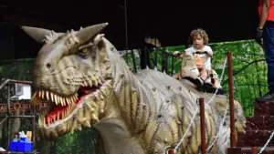 A small child rides a large animatronic dinosaur