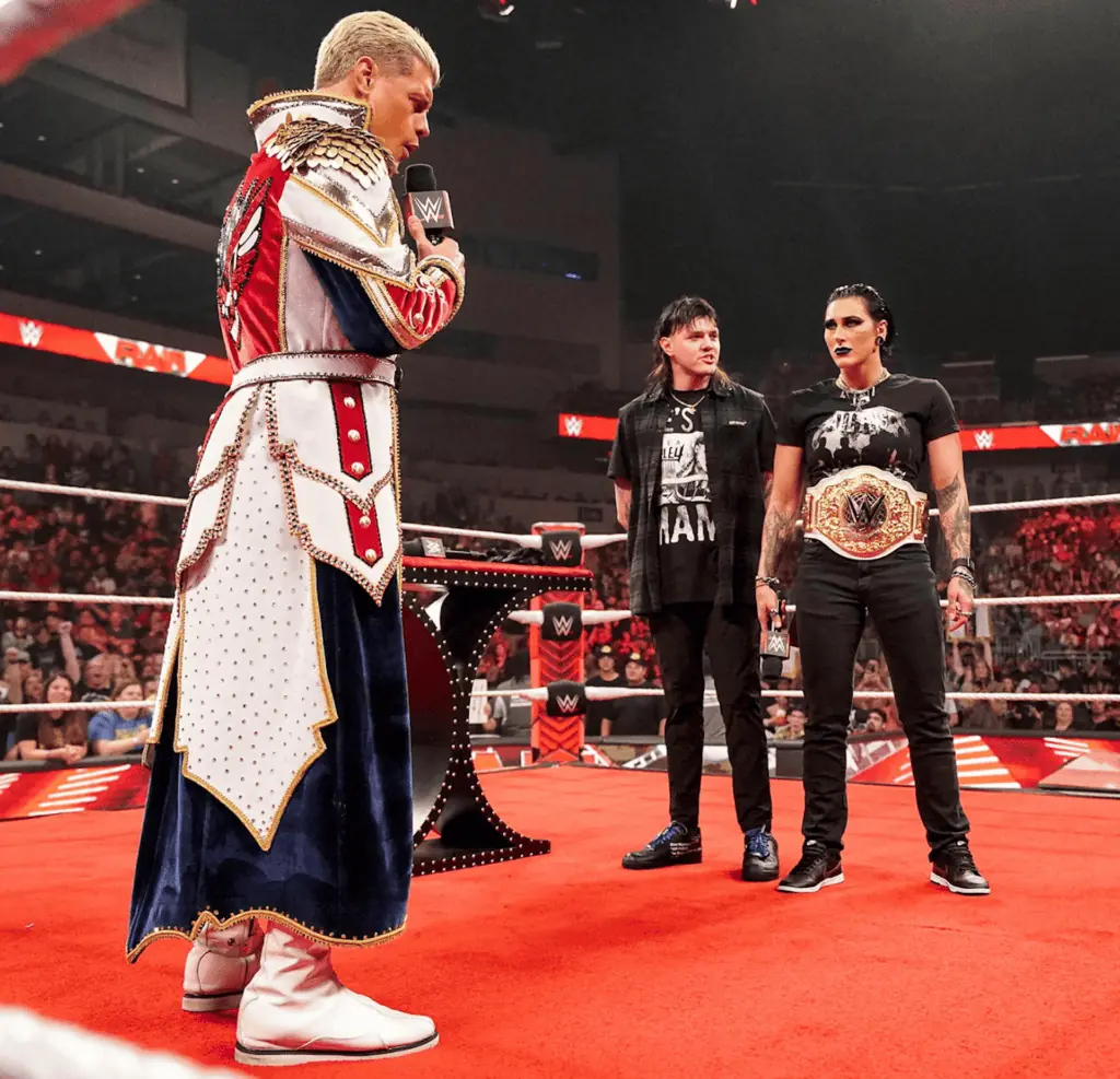 three people stand in a ring during a championship presentation ceremony