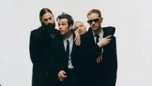 The 1975, a band, wearing black and white suits pose together in front of a white background