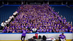 a group of people in purple shirts sit in blue bleacher seats and pose for a photo.