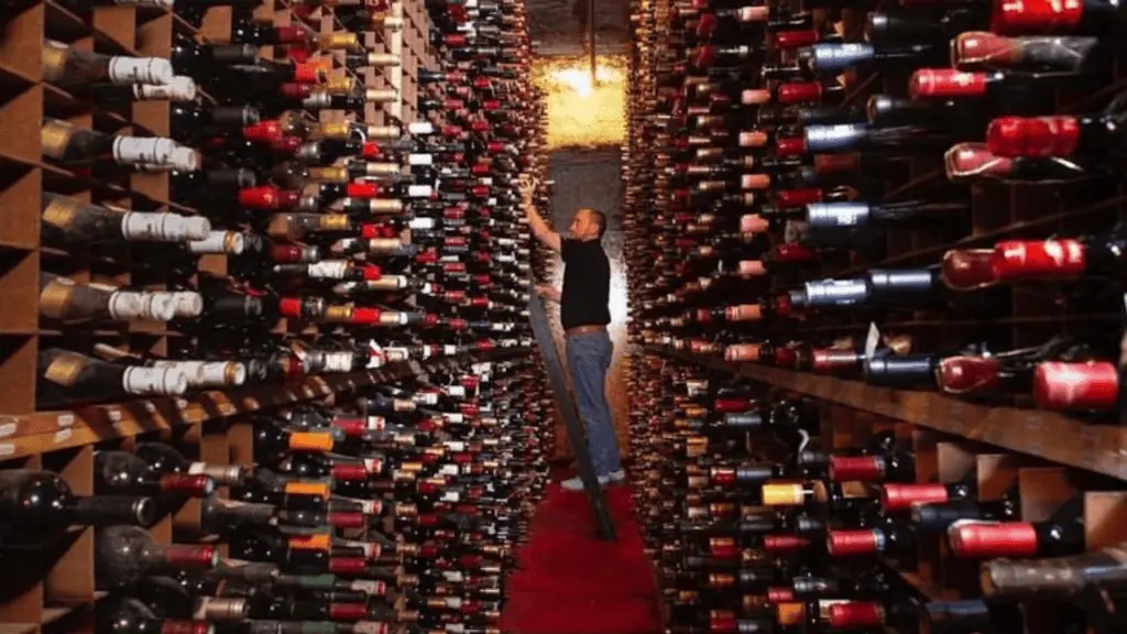 A giant wine cellar. a man looks through the bottles in the shelves.