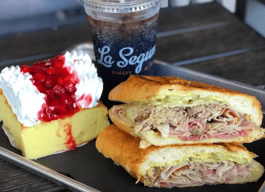 Cuban sandwich on a plate next to a slice of cake covered in guava sauce