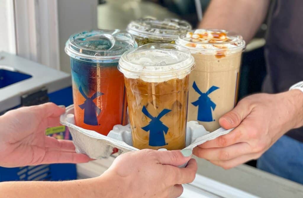 four frozen coffee drinks in a carrier being passed through a drive thru window