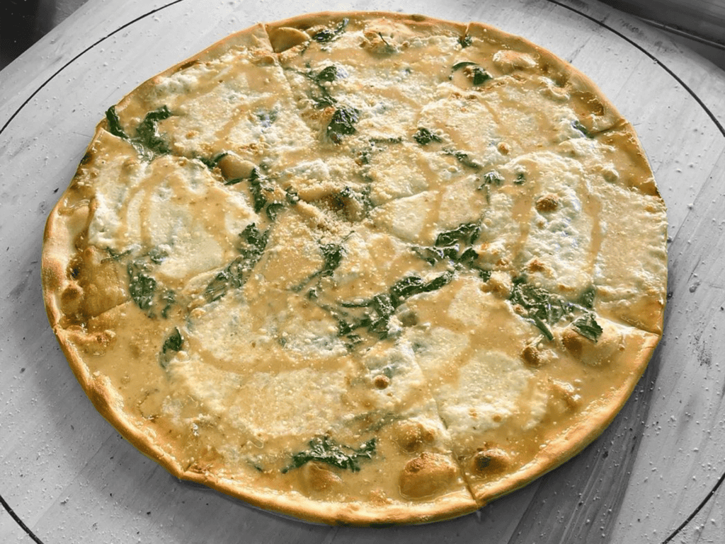 a Sicilian cream pizza on a table. Green garnishment is visible. 