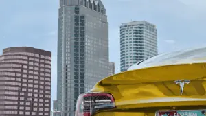 gold Tesla car photographed from the back with tall buildings in the background