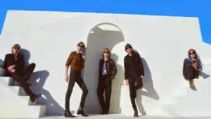 The band Phoenix posing on a white wall and stairs with blue sky behind it